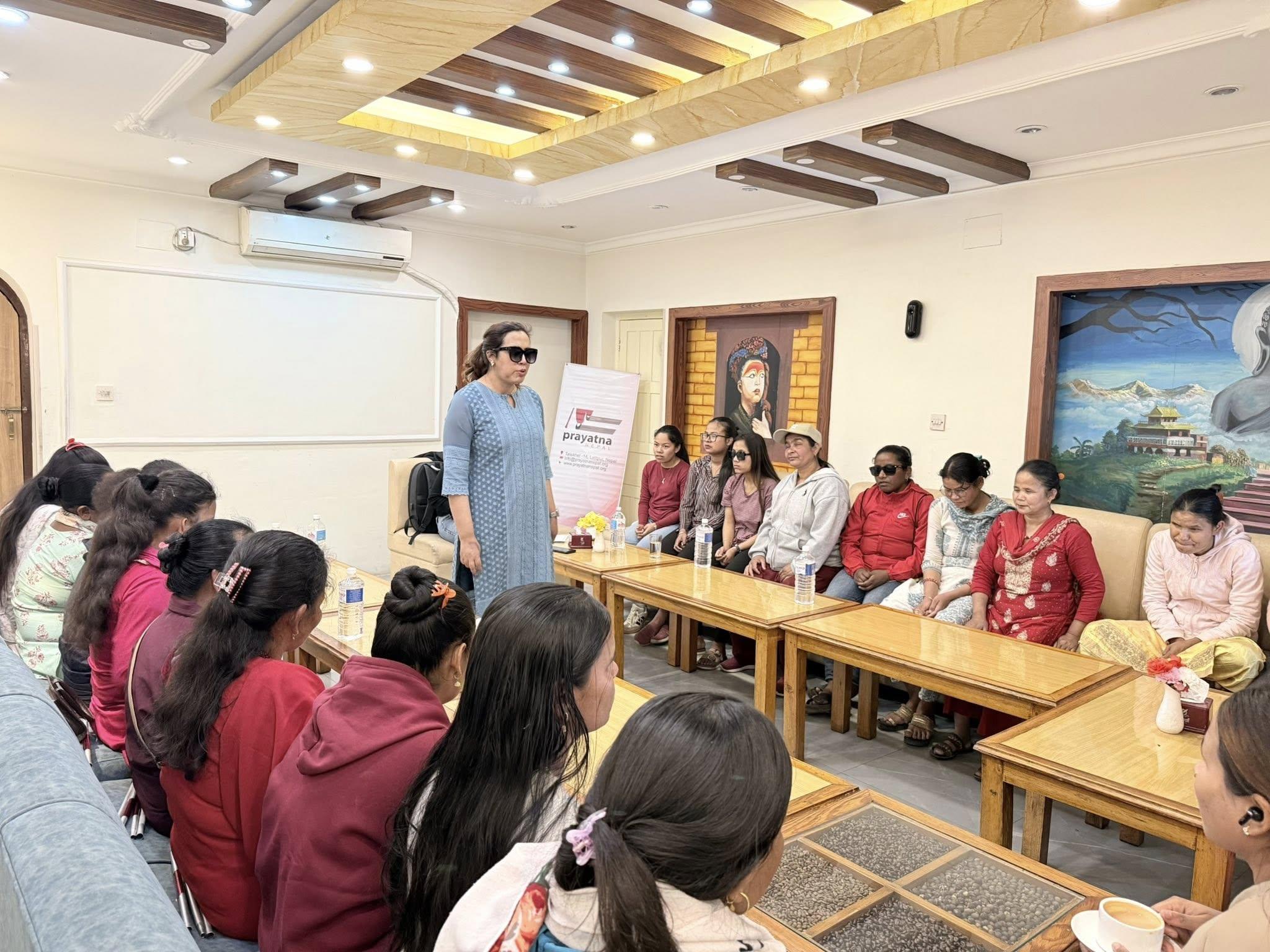 Sarita Lamichhane clad in blue kurta and sunglasses in her eyes facing the participants who are sitting down in U-style seating arrangement in chair and Prayatna Nepal Banner can be seen behind her.