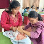 Two women touching baby mannequin with other people in a room.