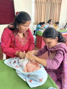 Two women touching baby mannequin with other people in a room.